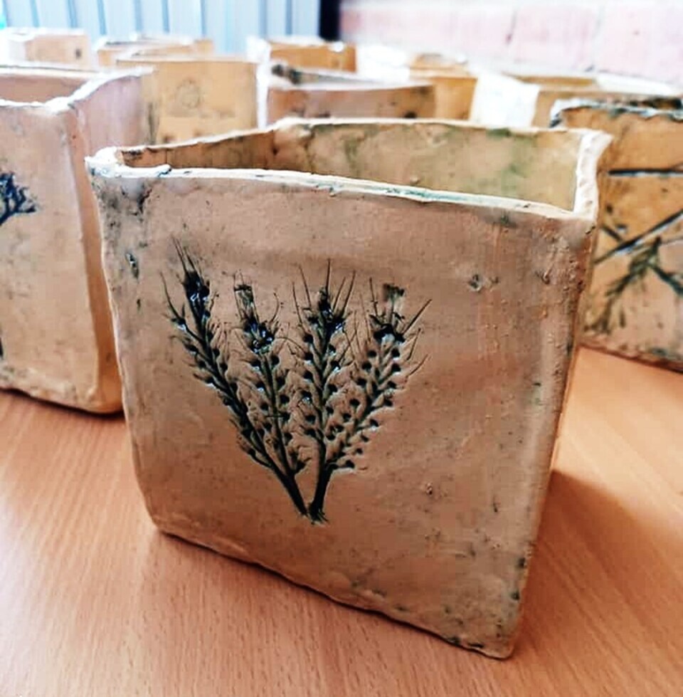 A handmade square ceramic pot with a pressed botanical design on the front, featuring stems and small flowers.